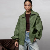 Person wearing a green jacket and blue jeans against a plain background